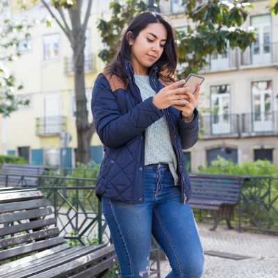 serious-woman-using-smartphone-standing-outdoors