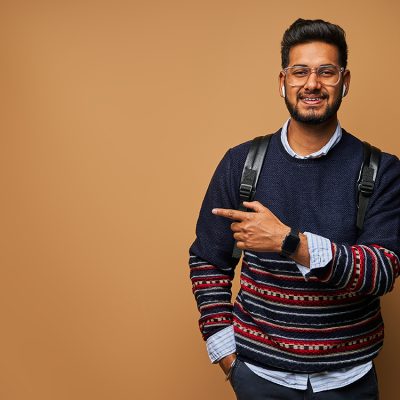 smiling-happy-indian-student-with-backpack-pointing-his-finger-wall