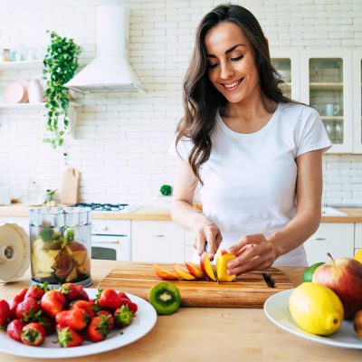 Beautiful woman making fruits smoothies with blender. Healthy ea